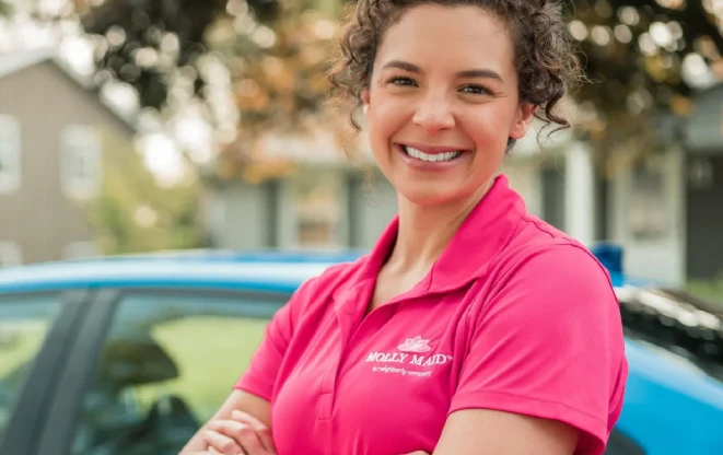 Smiling Molly Maid employee standing outside with her arms crossed.